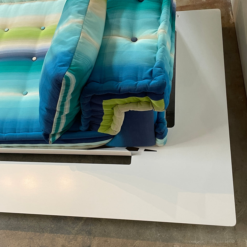 A modern, multicolored Roche Bobois Mah Jong Chaise Lounge from Roche Bobois with a gradient pattern in blue, green, and yellow shades, featuring a cushioned backrest and a matching pillow on a white base for perfect outdoor relaxation.