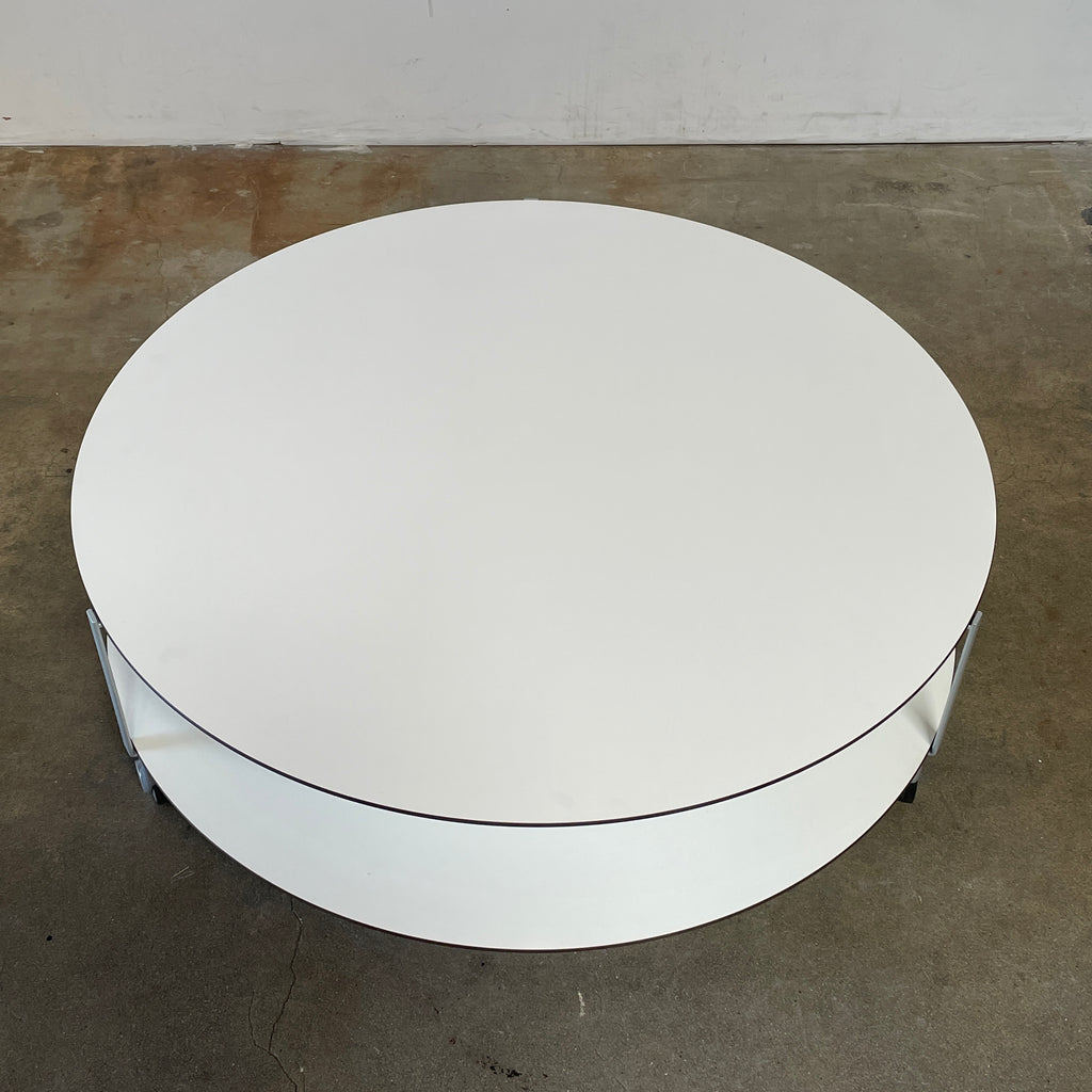 A Zanotta Giro Coffee Table, a round, white, two-tiered coffee table with a minimalist design, featuring a solid top and an open lower shelf for storage. The sleek steel frame adds durability, making it both stylish and functional.