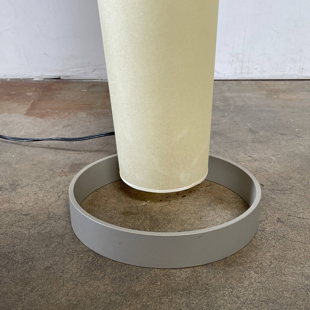 A modern, cone-shaped beige Pallucco Italia Abat Jour Floor Light by Pallucco Italia features a round base and a visible power cord, blending sleek design with Italian craftsmanship.