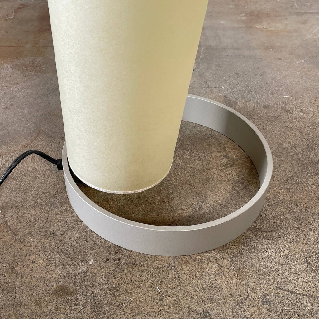 A modern, cone-shaped beige Pallucco Italia Abat Jour Floor Light by Pallucco Italia features a round base and a visible power cord, blending sleek design with Italian craftsmanship.