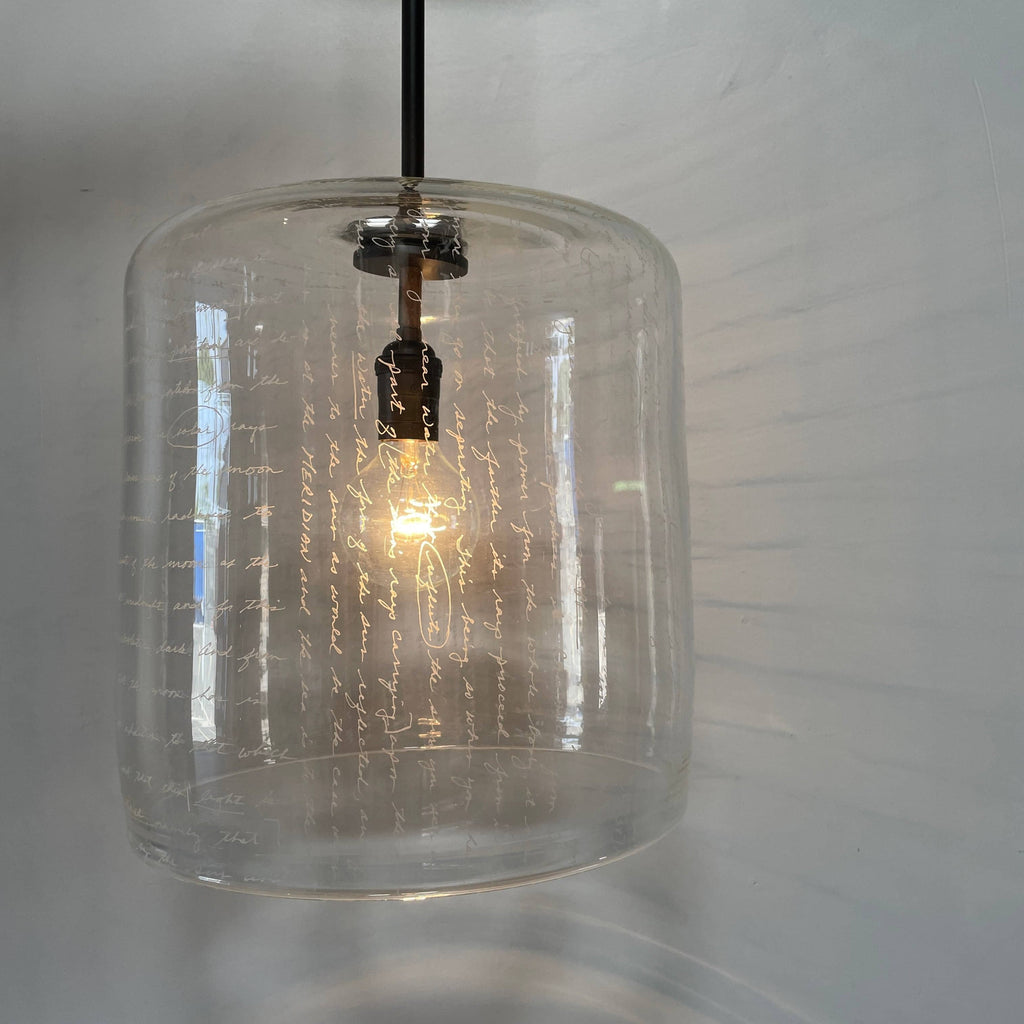 A unique functional art piece, this Alison Berger Word Pendant by Alison Berger showcases visible wires and mounting hardware against a white textured ceiling, reminiscent of Alison Berger's Word Pendant designs.