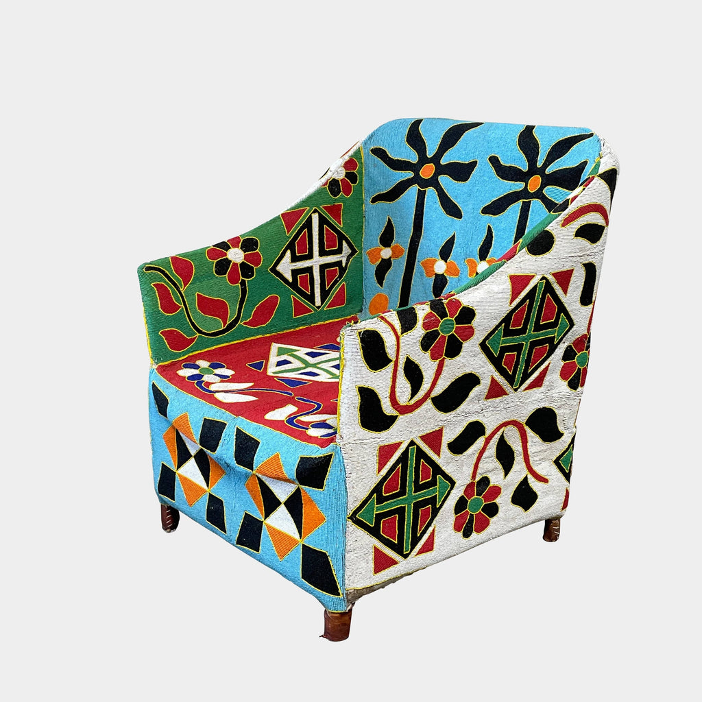 Introducing the Handmade Hand Beaded African Yoruba Chair, an armchair adorned with vibrant geometric and floral patterned fabric in red, green, blue, white, and black hues. This exquisite piece features wooden legs and a high backrest, capturing the essence of African-inspired design.