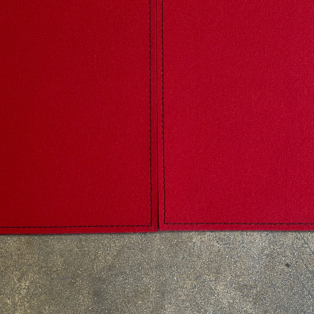 Close-up of the corner of a Large Felt Rug in a vibrant red color against a white background. The fabric showcases a clearly visible seam along its edge.