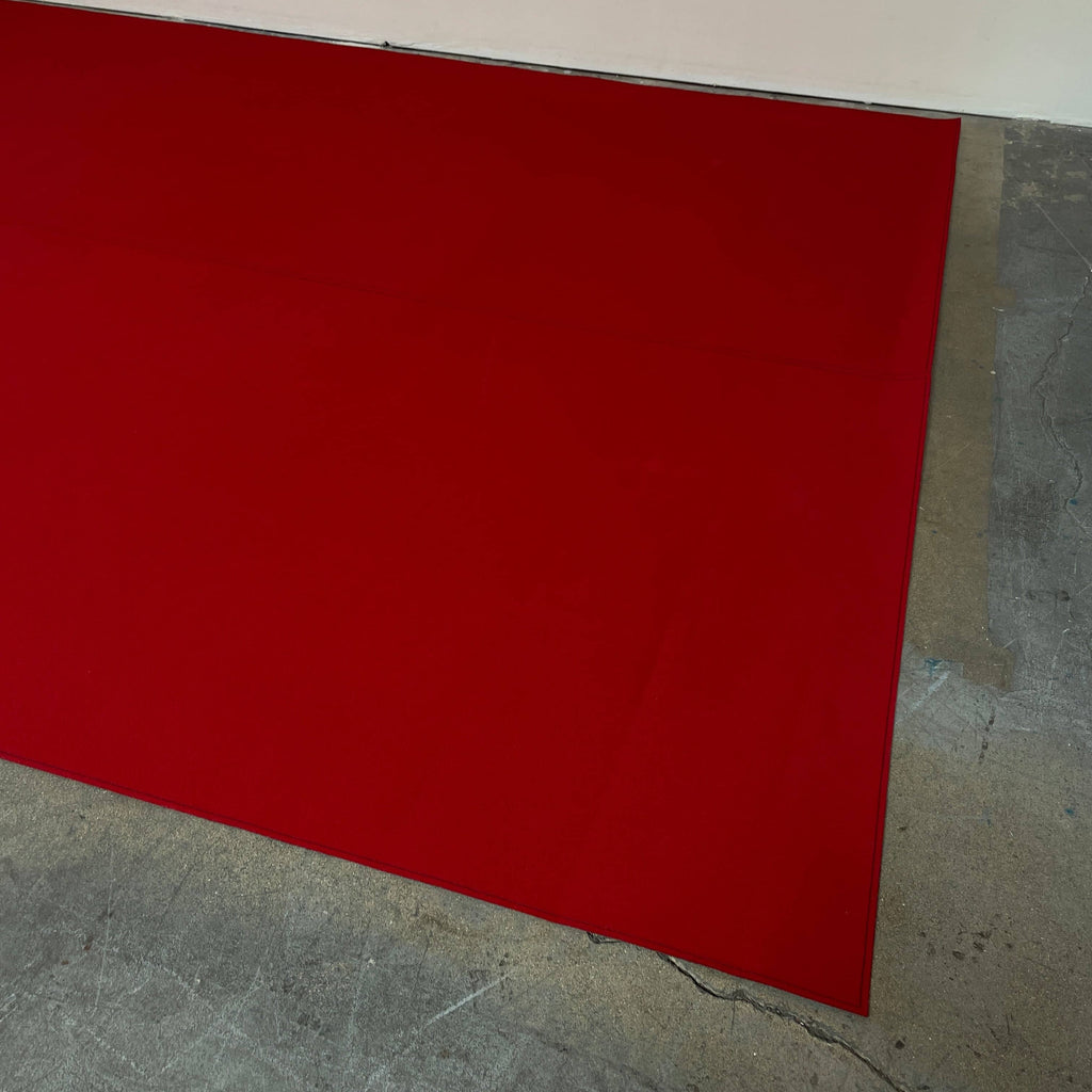 Close-up of the corner of a Large Felt Rug in a vibrant red color against a white background. The fabric showcases a clearly visible seam along its edge.