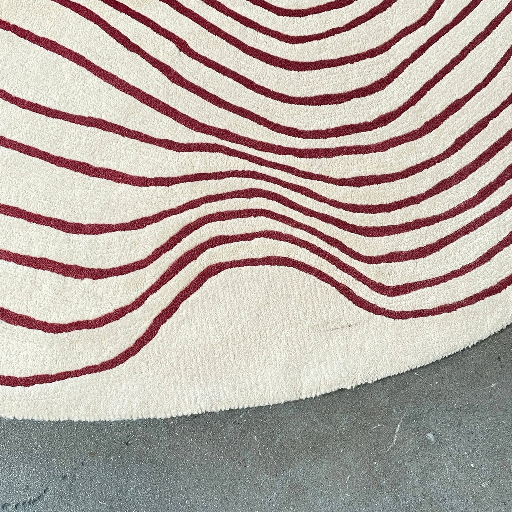 The Roche Bobois Volute Round Rug from Roche Bobois showcases a white surface decorated with red, wavy, parallel lines.