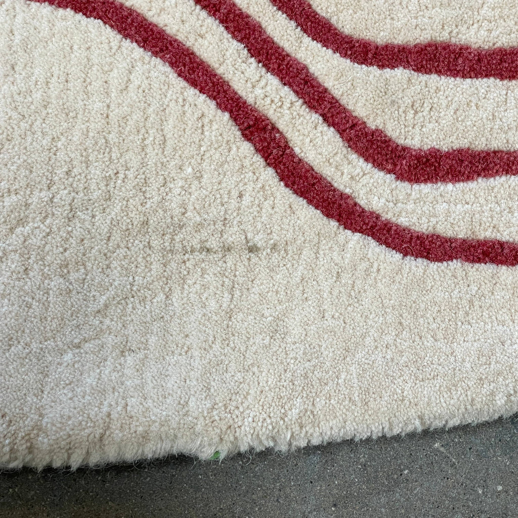 The Roche Bobois Volute Round Rug from Roche Bobois showcases a white surface decorated with red, wavy, parallel lines.