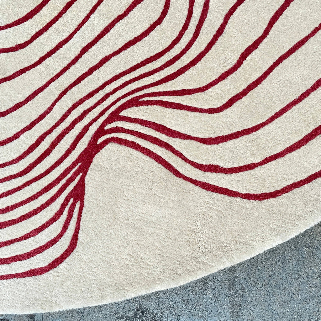 The Roche Bobois Volute Round Rug from Roche Bobois showcases a white surface decorated with red, wavy, parallel lines.