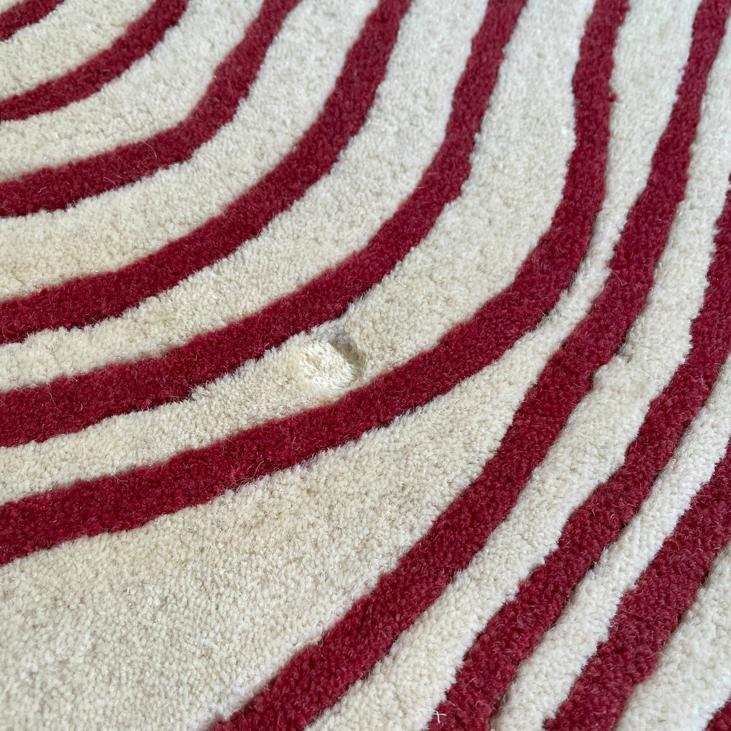 The Roche Bobois Volute Round Rug from Roche Bobois showcases a white surface decorated with red, wavy, parallel lines.