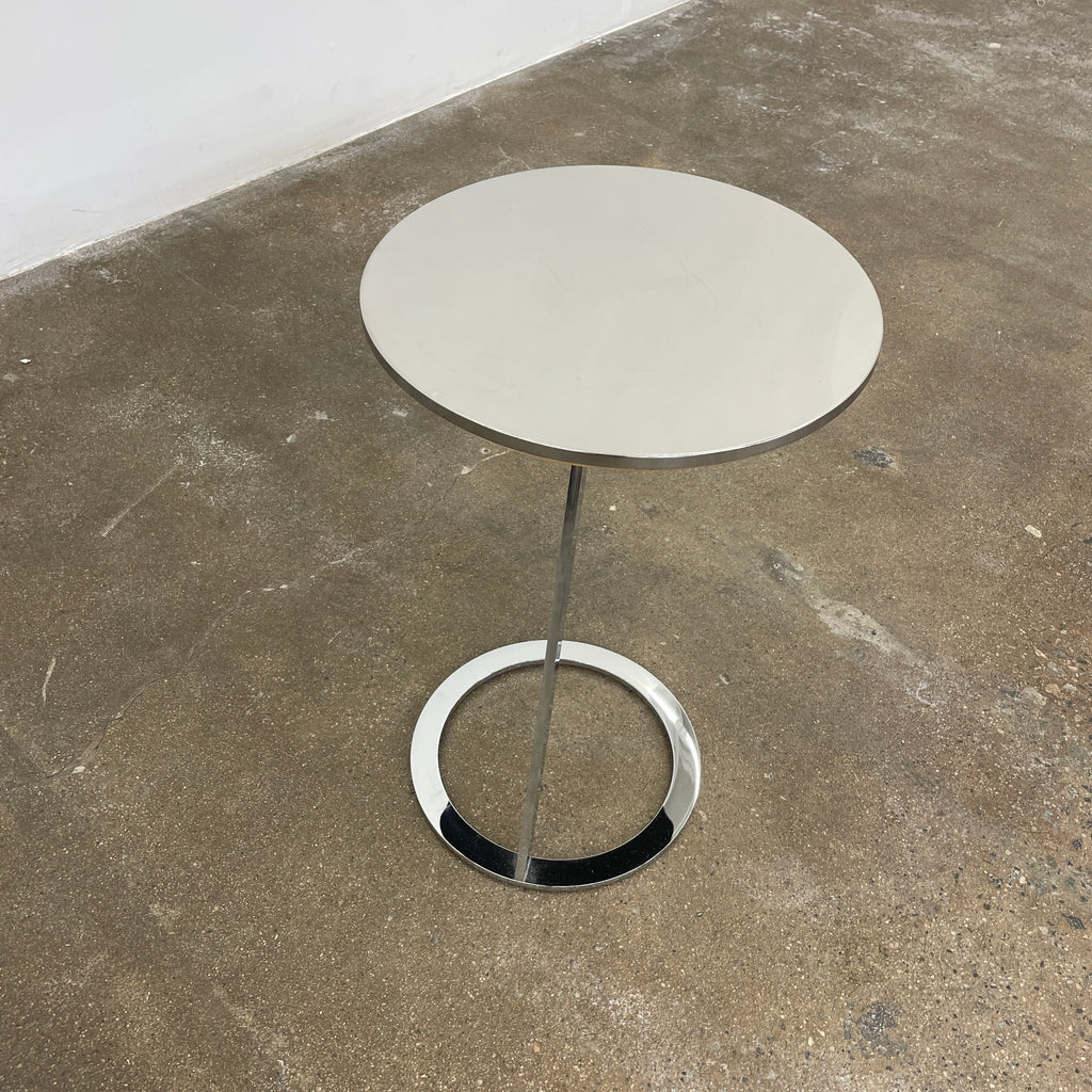 The Ligne Roset Good Morning Pedestal Side Table by Ligne Roset showcases a sleek, modern design with a round top and a distinctively angled chrome metal base on a circular foot.