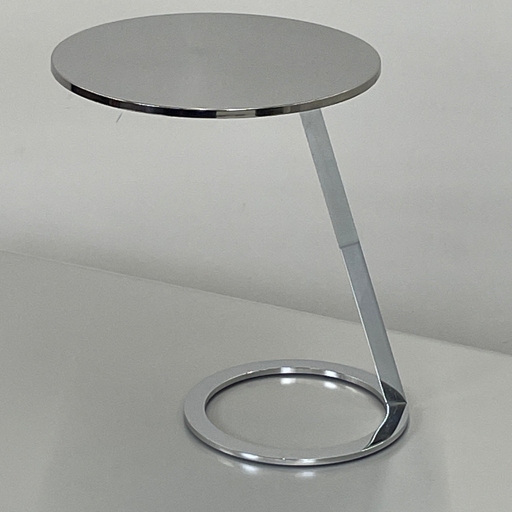 The Ligne Roset Good Morning Pedestal Side Table by Ligne Roset showcases a sleek, modern design with a round top and a distinctively angled chrome metal base on a circular foot.