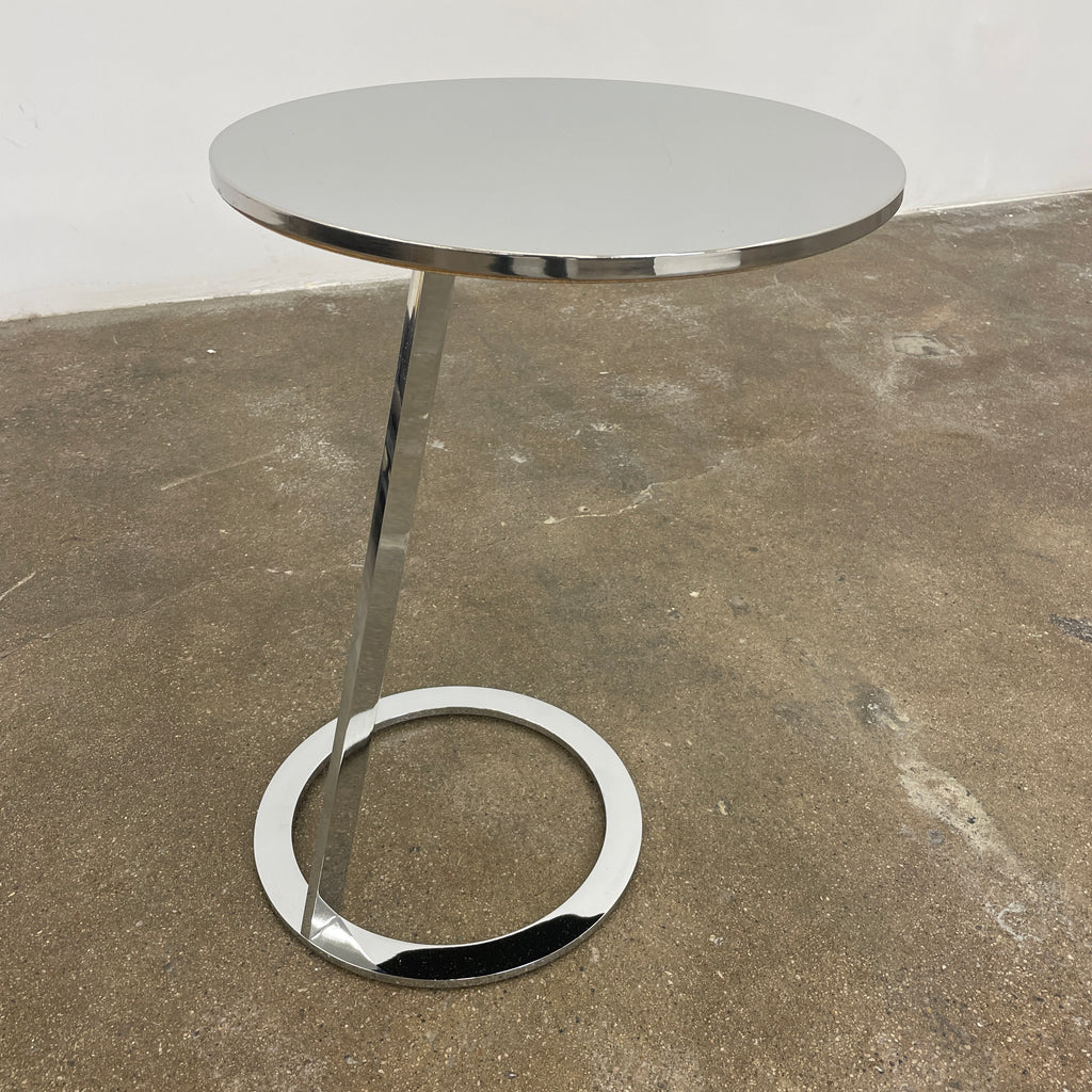 The Ligne Roset Good Morning Pedestal Side Table by Ligne Roset showcases a sleek, modern design with a round top and a distinctively angled chrome metal base on a circular foot.