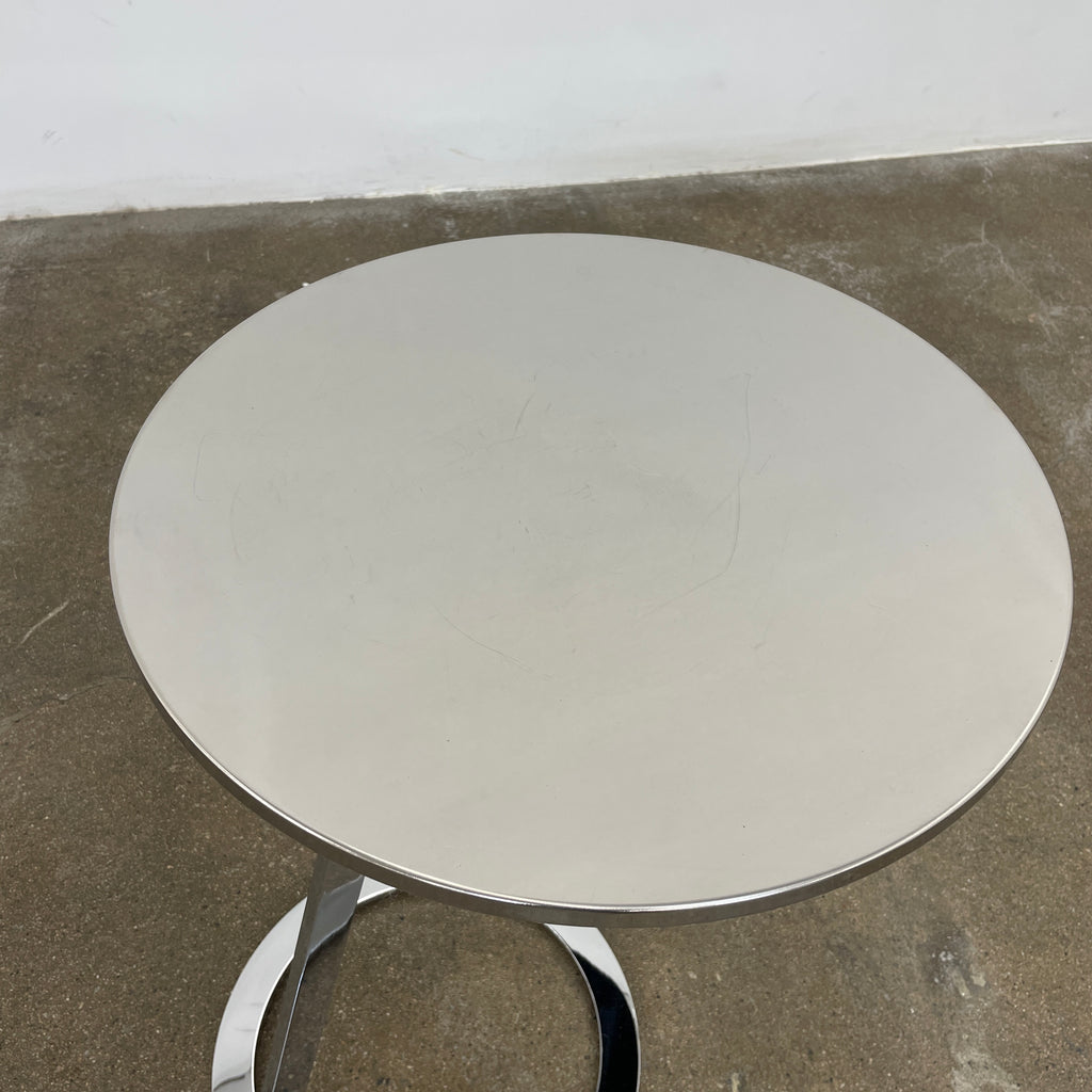 The Ligne Roset Good Morning Pedestal Side Table by Ligne Roset showcases a sleek, modern design with a round top and a distinctively angled chrome metal base on a circular foot.