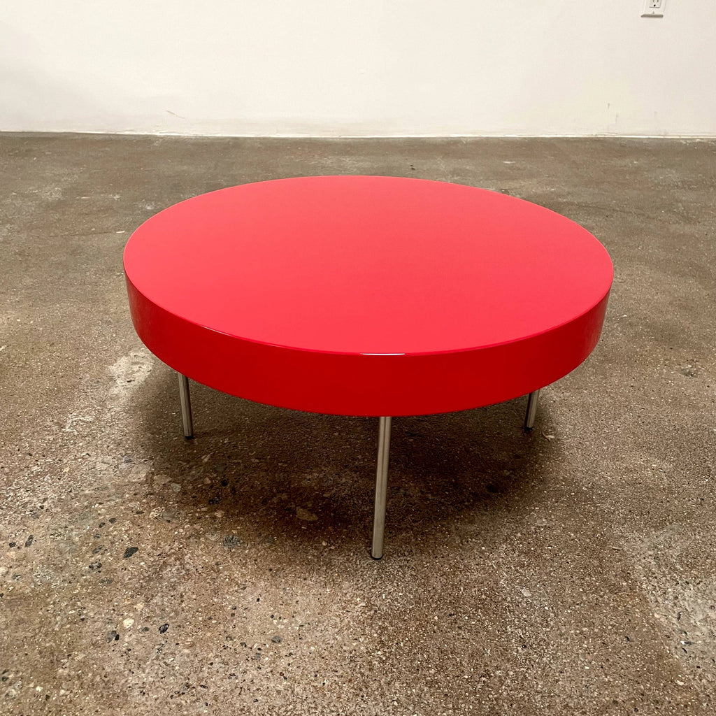 A Ligne Roset Red Lacquer Needle Table with a glossy red surface and four slim metal legs sits on a plain white background, capturing the essence of modern elegance characteristic of Ligne Roset designs.