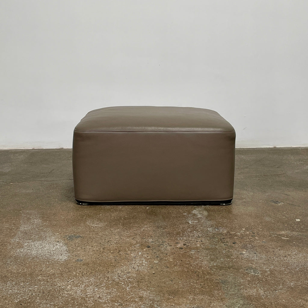 The Minotti Davis Leather Ottoman is a luxurious square piece crafted from rich brown leather, beautifully contrasted with a pristine white background.