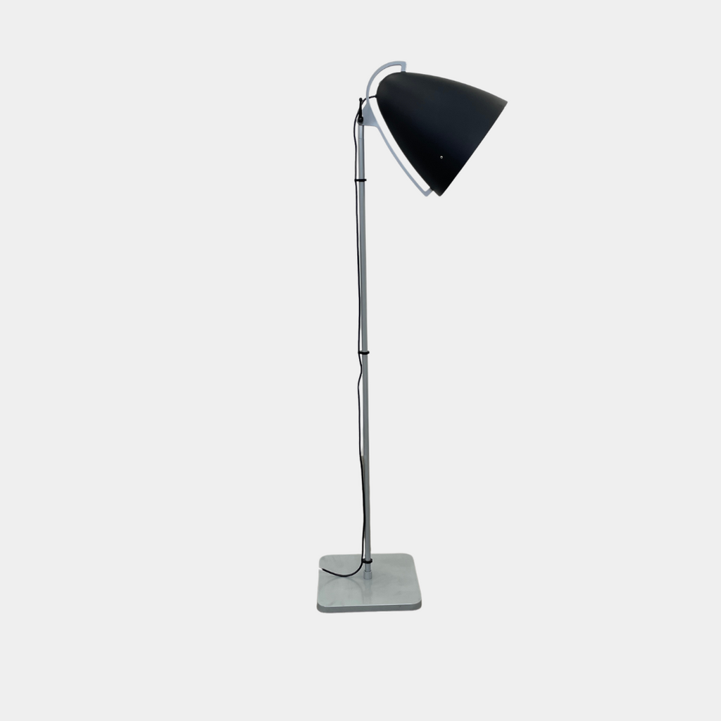 The Pallucco Italia Faro Floor Lamp, featuring a round, cone-shaped shade and set on a square base, exudes industrial design in a minimal room with a concrete floor.