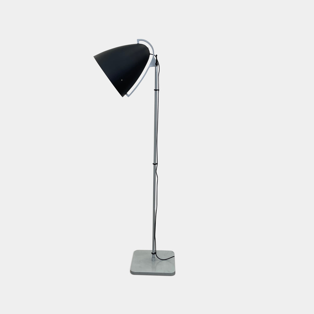 The Pallucco Italia Faro Floor Lamp, featuring a round, cone-shaped shade and set on a square base, exudes industrial design in a minimal room with a concrete floor.