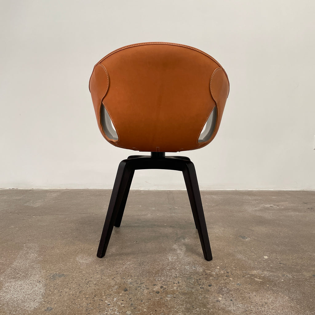 Introducing the Poltrona Frau Small Ginger Chair, a modern piece from the renowned brand Poltrona Frau. It boasts a gray leather seat with brown trim, featuring an open back design and supported by four sleek black legs, making a sophisticated statement on any concrete floor.