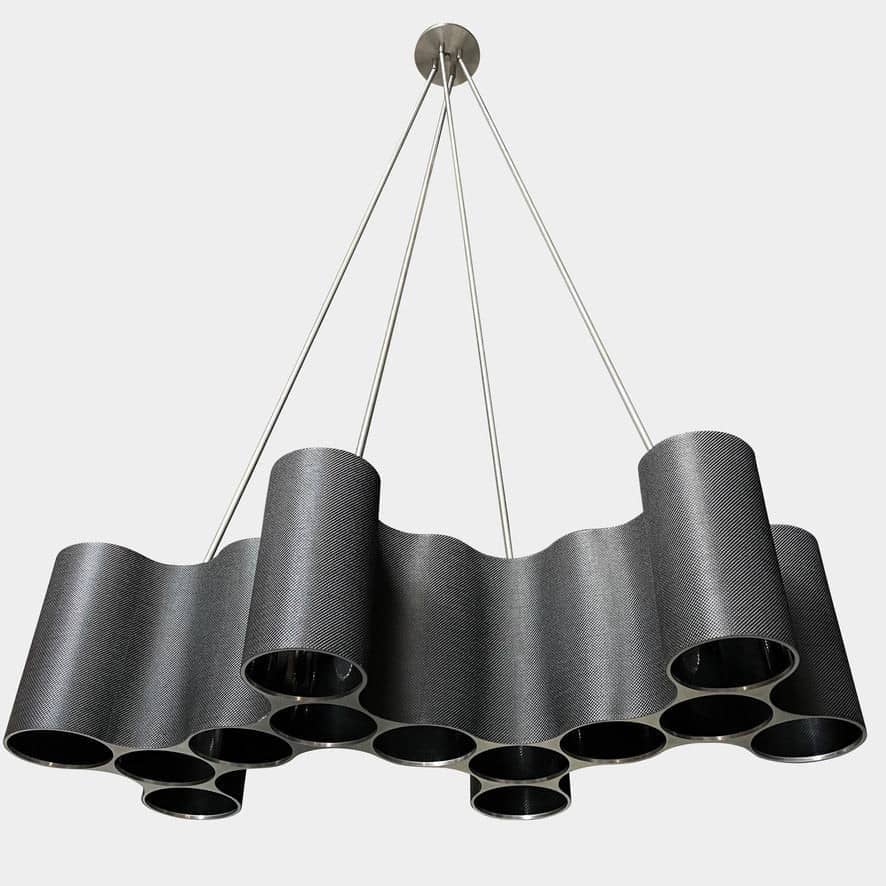 A modern metal chandelier with multiple cylindrical shades connected by thin, curved attachments, hanging from a ceiling mount—a design reminiscent of the Ralph Pucci Linear Cumulus Ceiling Light.