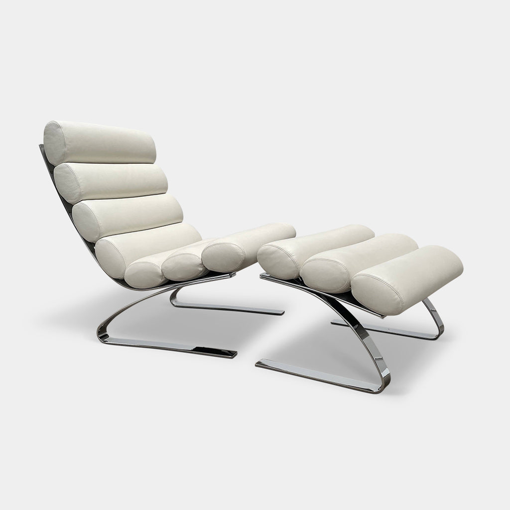 The COR Sinus Lounge Armchair and Ottoman by COR in polar white leather features a distinctive cylindrical cushion design and a chrome-plated frame, creating a striking presence on a concrete floor against a plain wall.