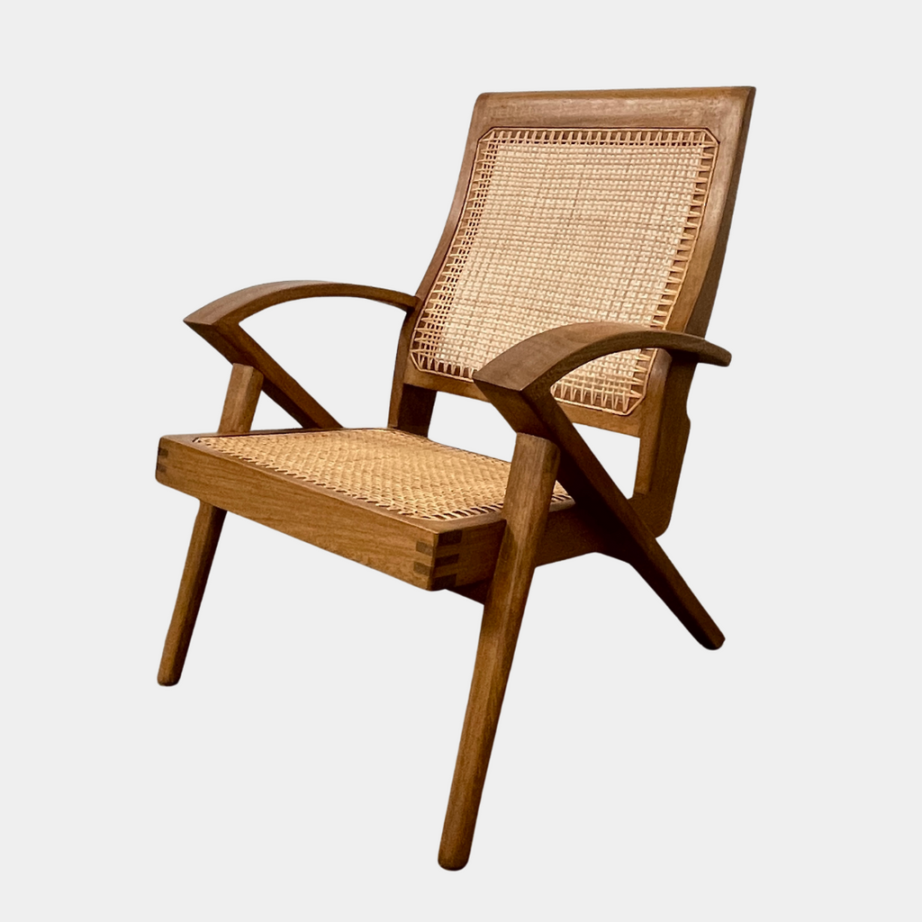 The Claude Home Teak Rex Armchair showcases a sophisticated design with a teak wood frame and a woven rattan seat and backrest, offering a gently reclined silhouette. It stands elegantly on a concrete floor against a plain wall, emanating the timeless charm characteristic of the Claude Home collection.