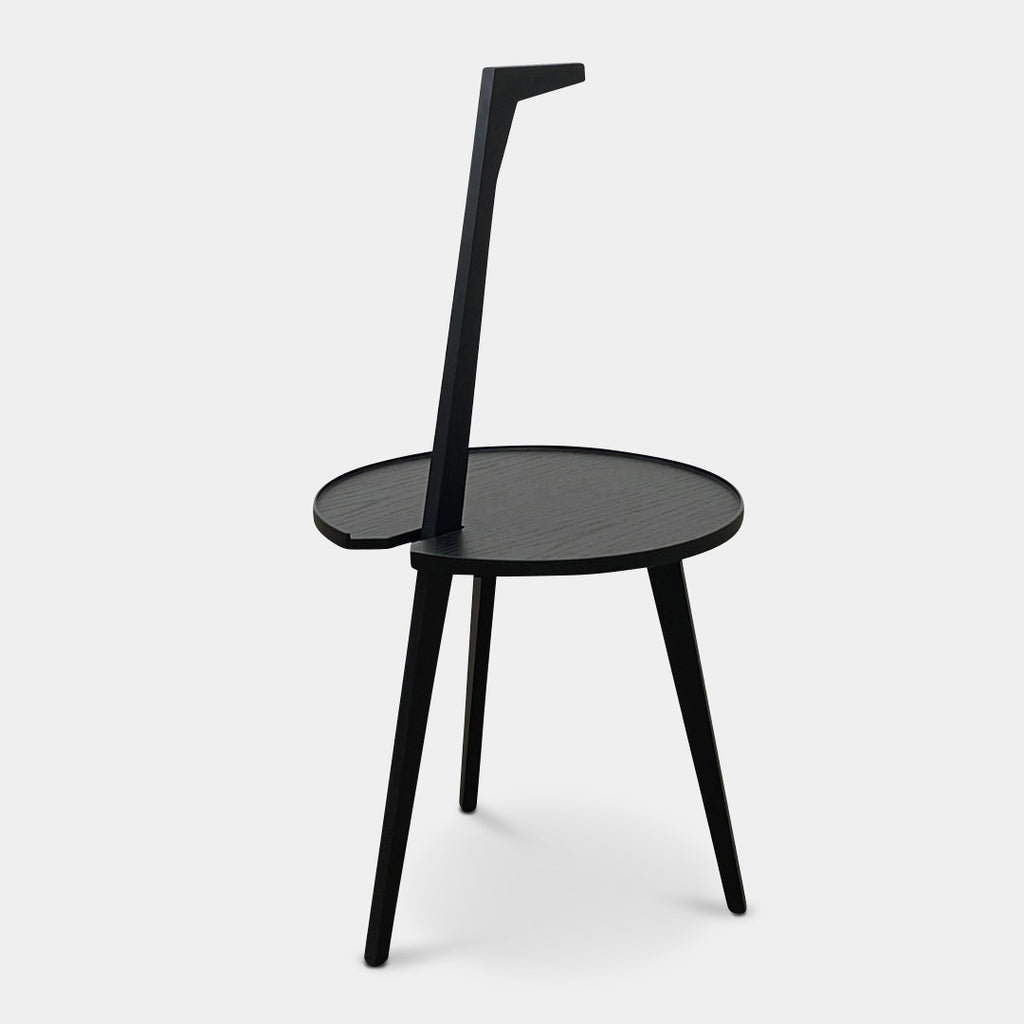 The Cassina Cicognino Side Table by Cassina is black and modern, featuring a round top, three legs, and a vertical handle-like design.